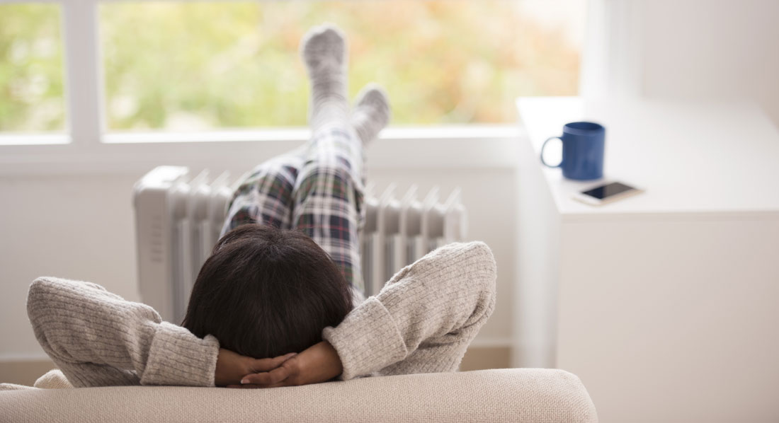 Eine Frau sitzt entspannt auf einem Sofa und hat ihre Beine auf einem Heizkörper ausgestreckt