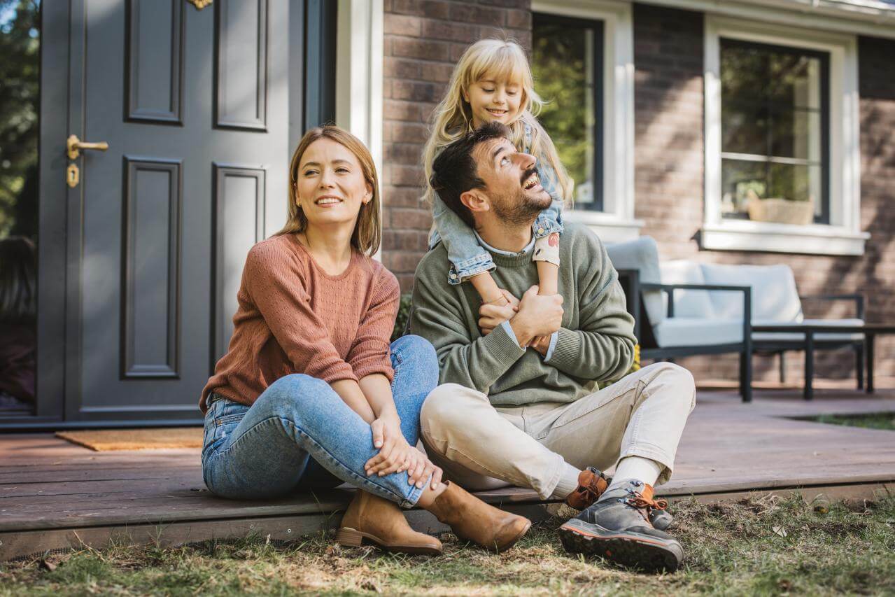 Familie mit Kind sitzt auf Veranda und denkt darüber nach ihr Einkommen abzusichern