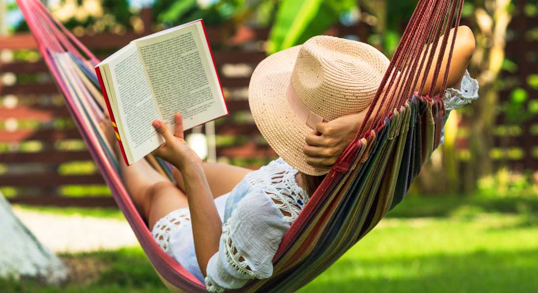 Eine Frau mit Hut liegt entspannt in der Hängematte und liest ein Buch