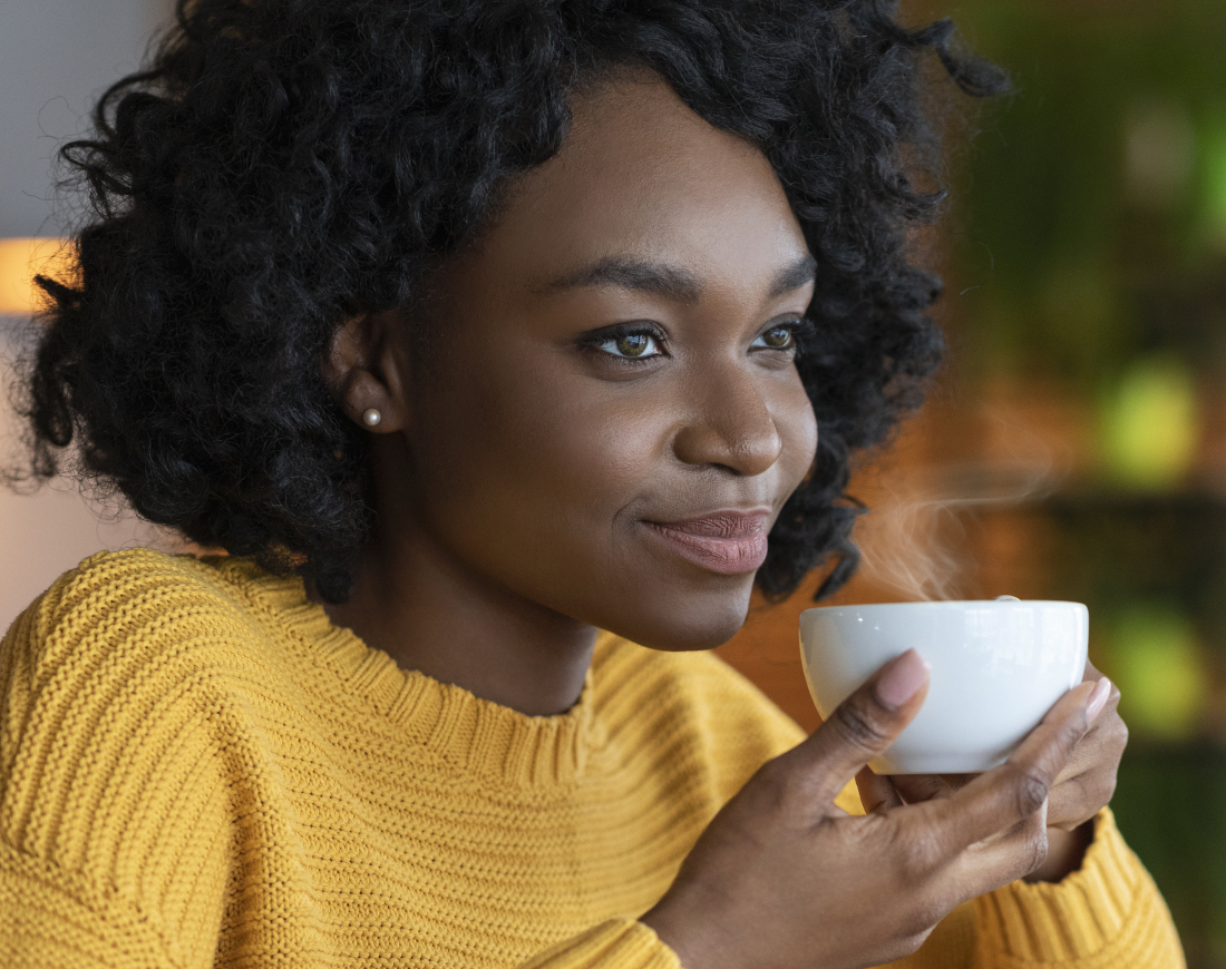 Eine zuversichtlich blickende Frau hält eine Kaffeetasse in den Händen