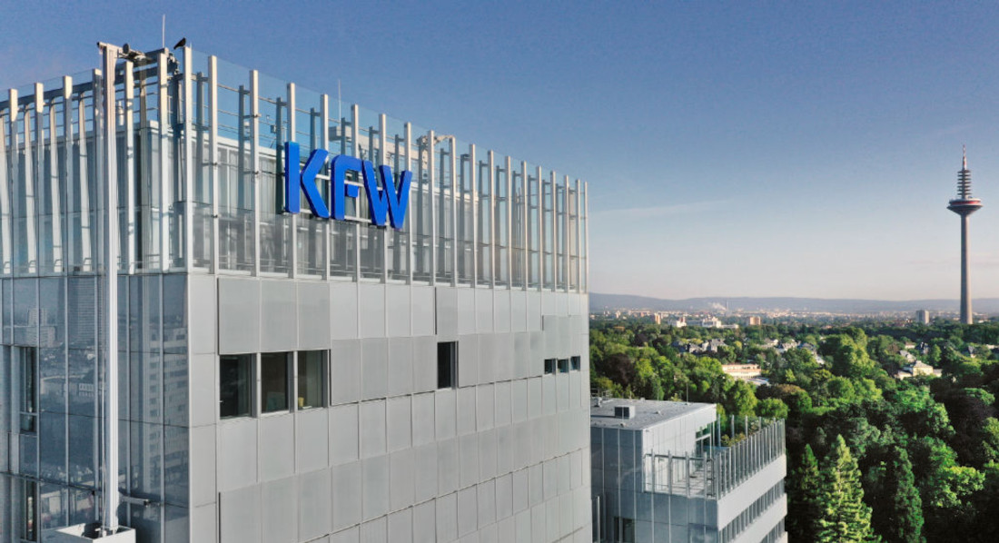 Ansicht des KfW-Hauptgebäudes in Frankfurt am Main. Man sieht ein großes Glasgebäude im Sonnenuntergang. An der Fassade ein blaues KfW-Logo.