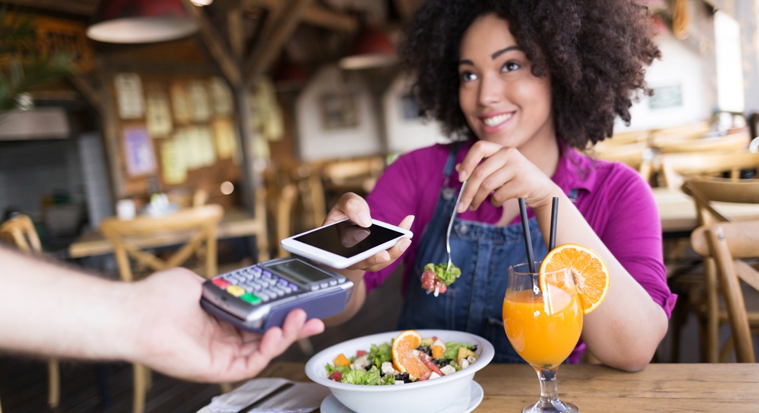 Frau bezahlt am Tisch im Restaurant einen Salat, indem sie ihr Handy über ein Lesegerät hält.