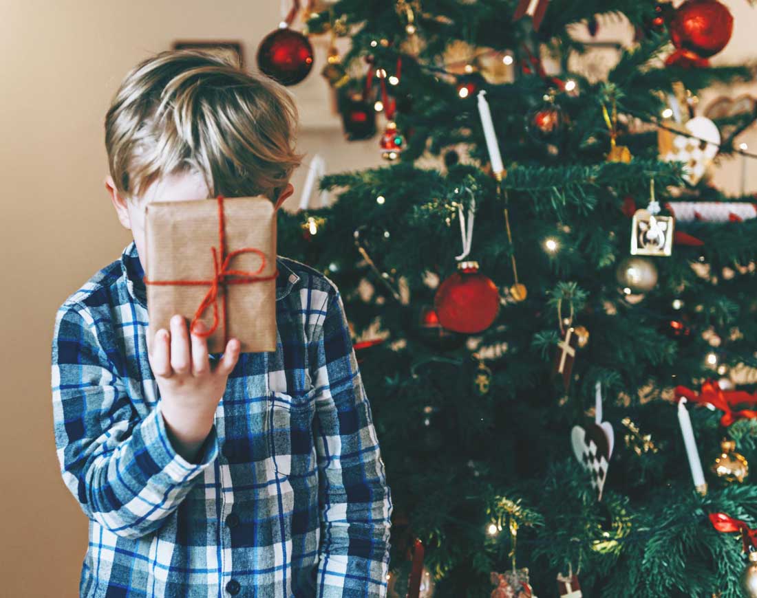 Junge im Schlafanzug presst sich ein noch verpacktes Weihnachtsgeschenk gegen die Stirn
