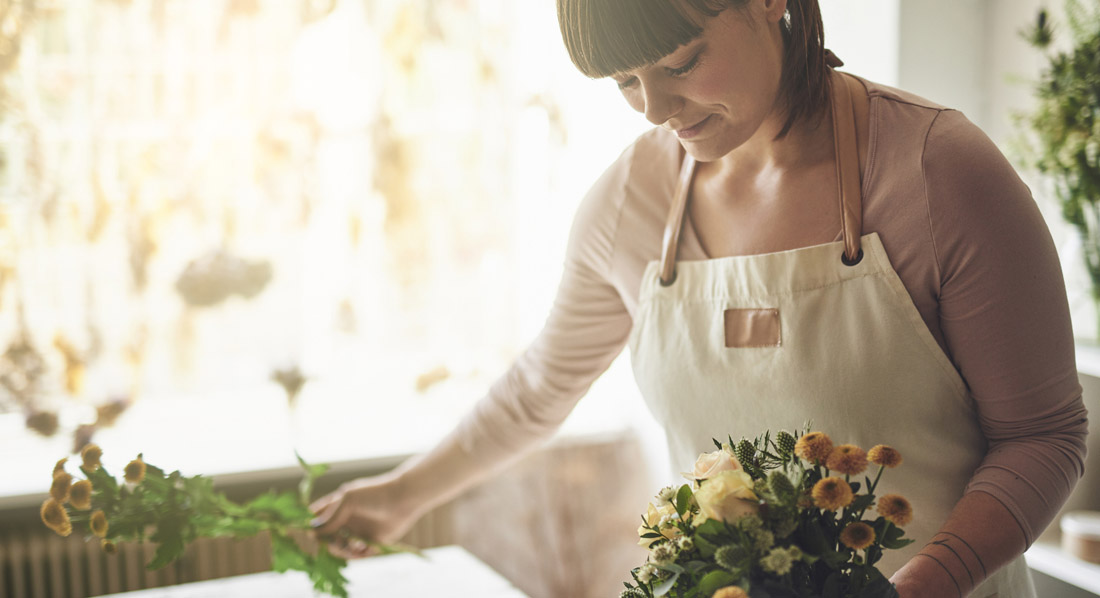 Eine junge Frau steht an einem Tisch und bindet Blumen zu einem Strauß