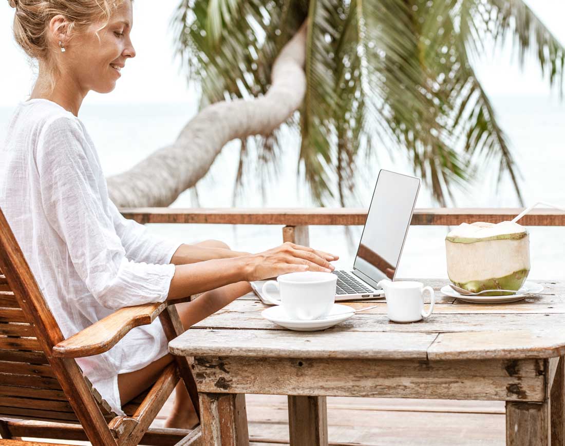 Eine junge Frau arbeitet am Laptop auf einer Terrasse am Meer