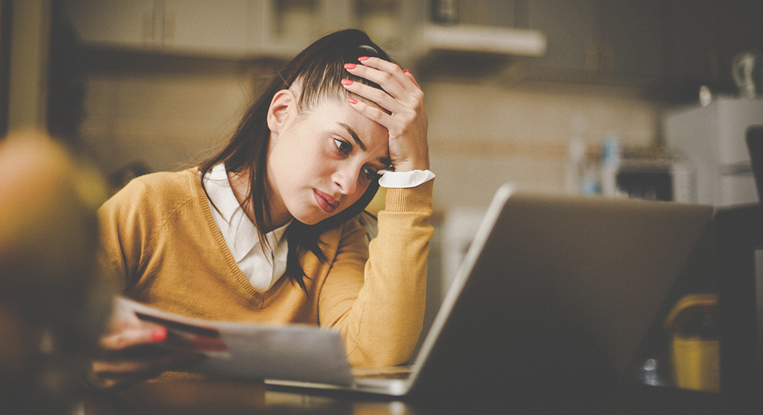 Junge Frau sitzt verzweifelt mit Kreditkarte und Unterlagen vor ihrem Laptop