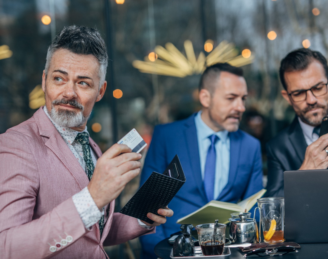 Ein Geschäftsmann zahlt im Restaurant mit Kreditkarte, im Hintergrund sind zwei weitere Männer ins Gespräch vertieft Download-Link:
