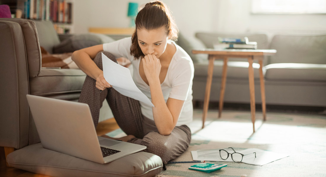 Eine Frau sitzt nachdenklich mit einer Rechnung am Laptop