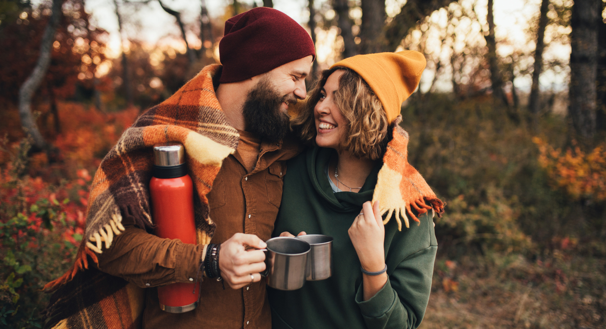 Ein Mann und eine Frau sind in der Natur, umarmen sich und haben Tassen in der Hand