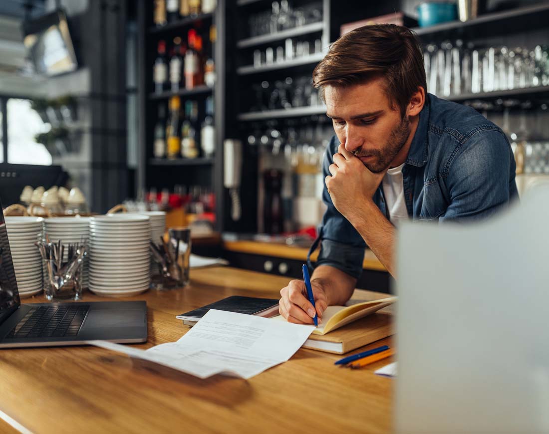 Der Besitzer eines Cafés stützt sich auf den Tresen und rechnet Beträge zusammen