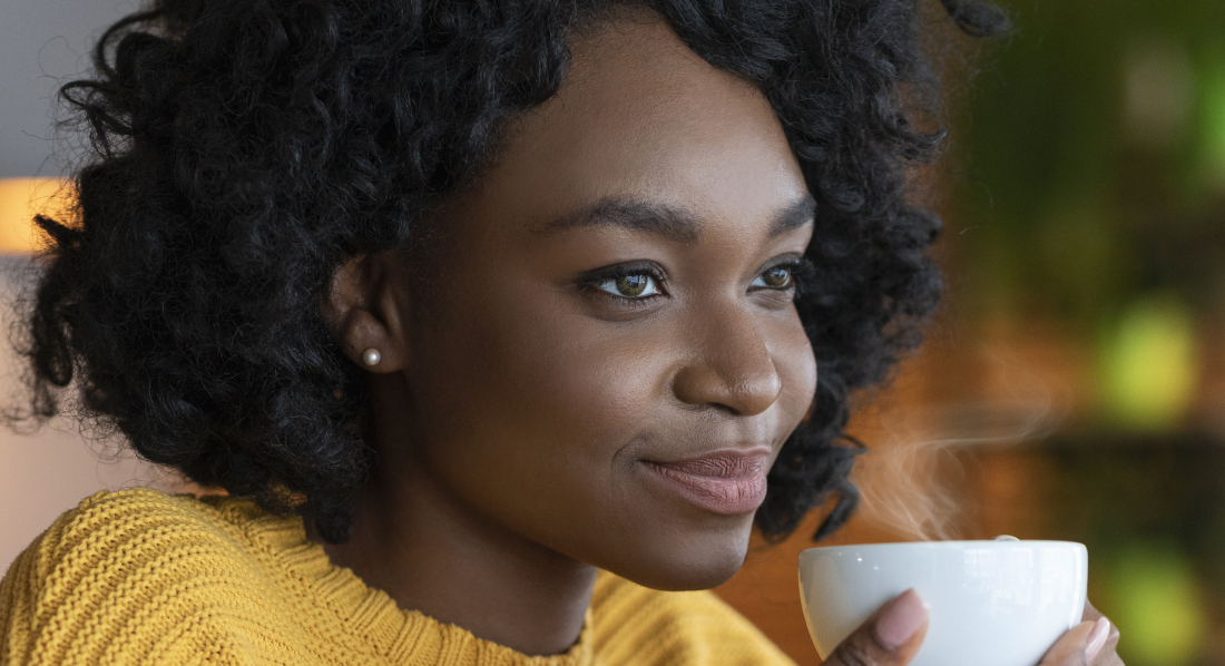 Eine zuversichtlich blickende Frau hält eine Kaffeetasse in den Händen