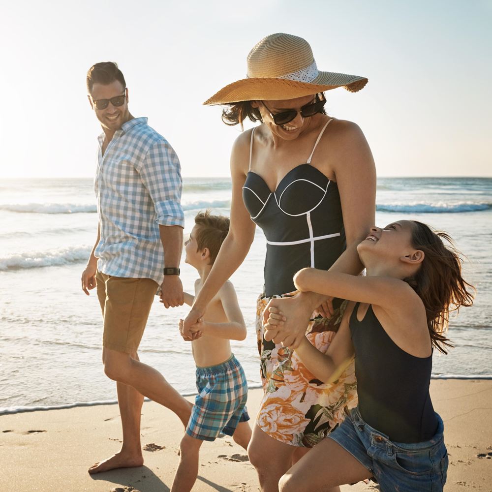 Ein Familie mit 2 Kindern spaziert am Strand und freut sich über ihre Traumreise, die sie mit den Vorteilen der Kreditkarte der Hanseatic Bank gebucht hat