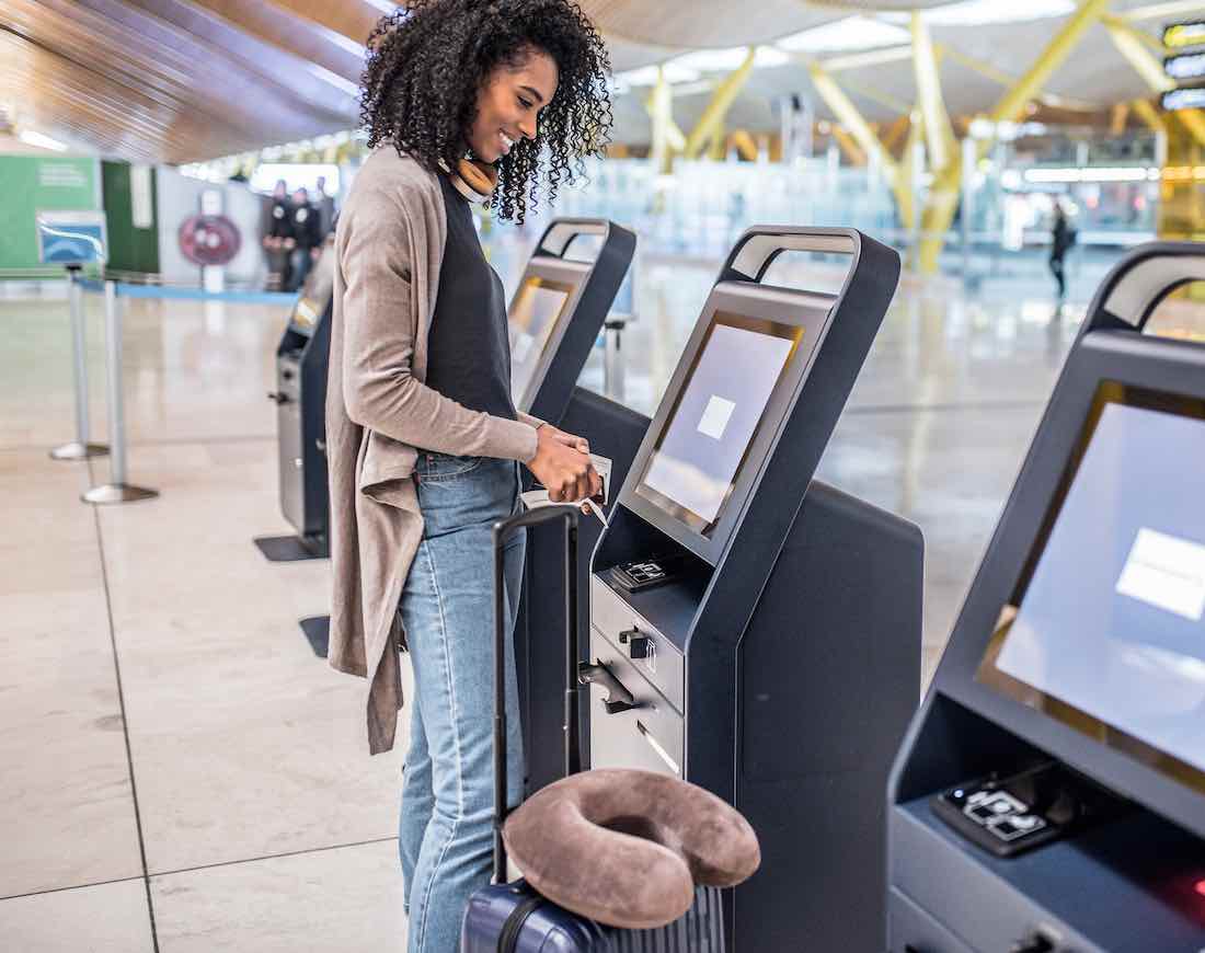Junge Frau beim Geld abheben im Ausland, im Hintergrund ein Flughafen-Terminal.