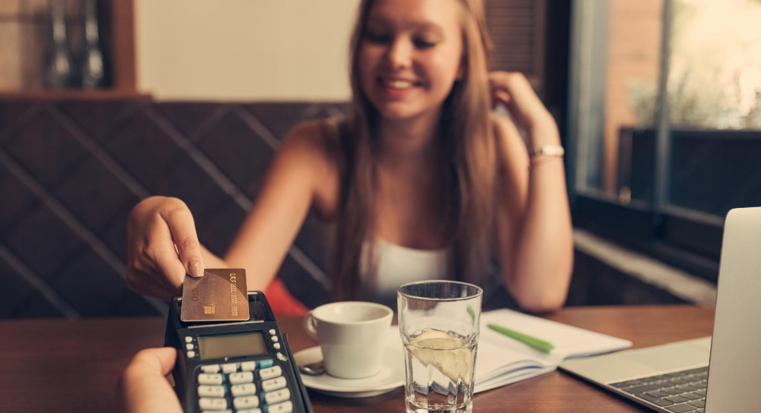 Eine Teenagerin bezahlt in einem Bistro ihren Kaffee mit einer Kreditkarte