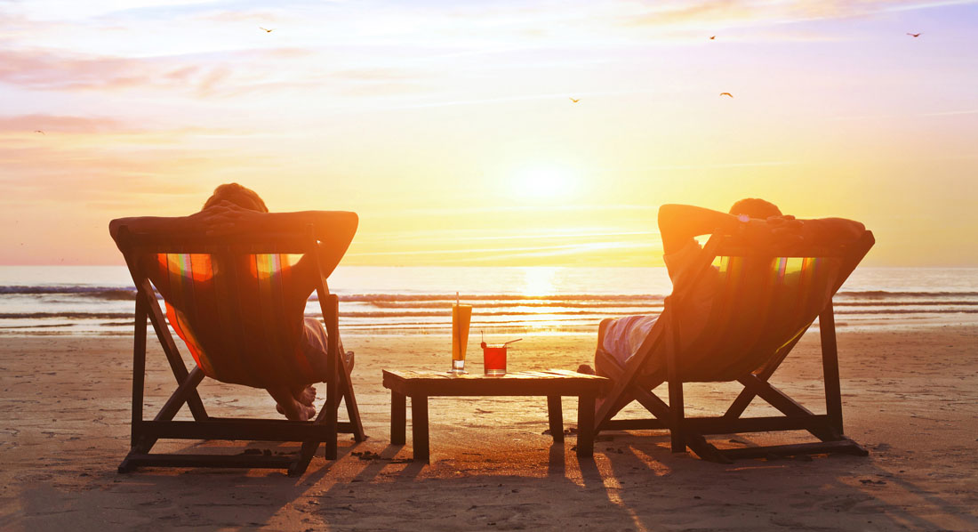 Ein Paar sitzt in Liegestühlen am Strand und verfolgt entspannt den Sonnenuntergang
