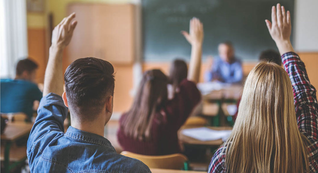 Erwachsene Schüler in einem Klassenraum heben den Arm, um eine Frage zu beantworten