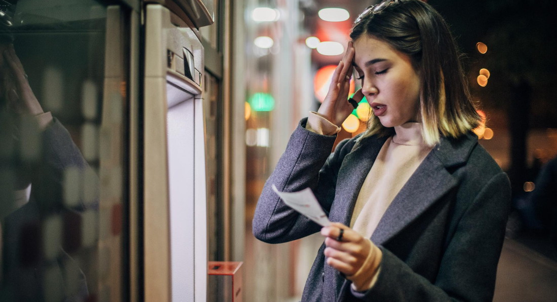 Junge Frau steht nach dreimaliger falscher PIN-Eingabe entnervt an einem Geldautomaten