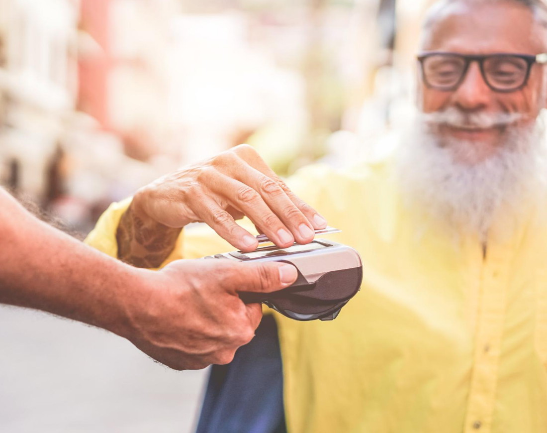 Ein Mann in einem Straßencafé legt gut gelaunt eine Kreditkarte mit NFC-Funktion auf ein Lesegerät