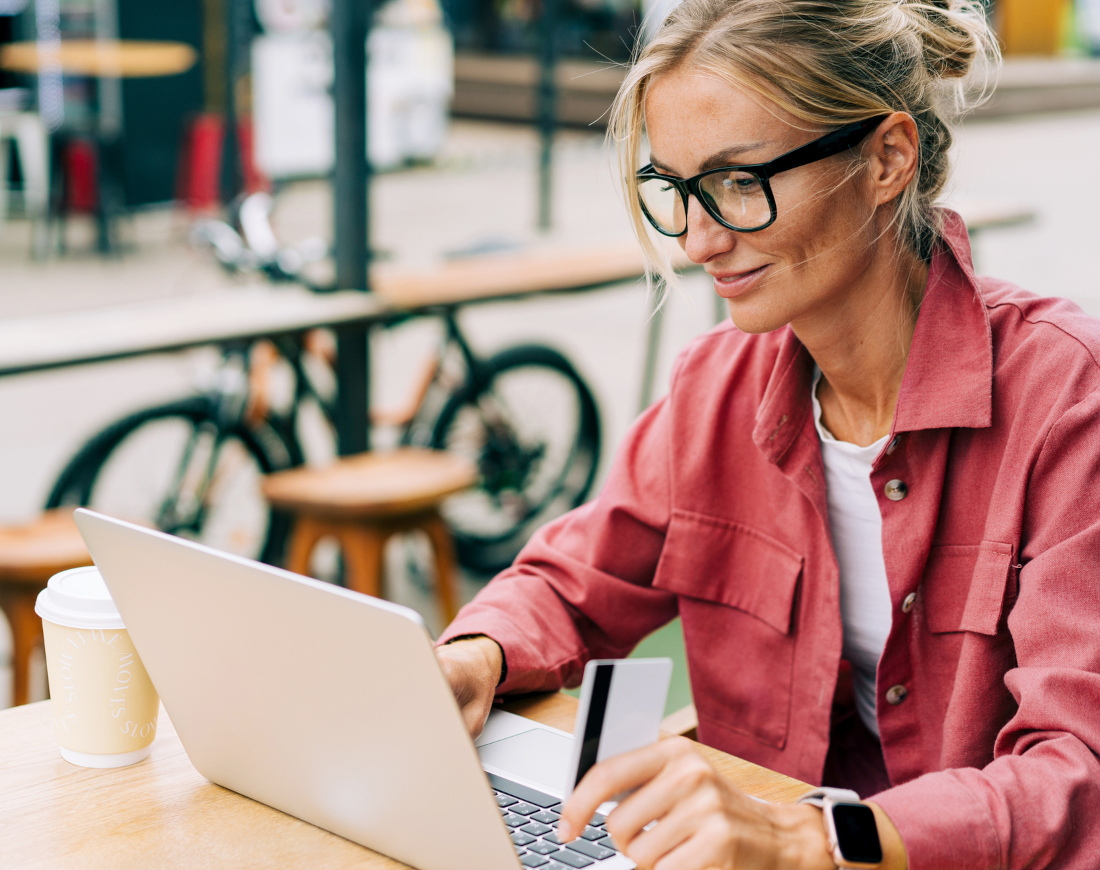 Eine Frau sitzt in einem Café und arbeitet mit einer Bezahlkarte in der Hand an einem Laptop