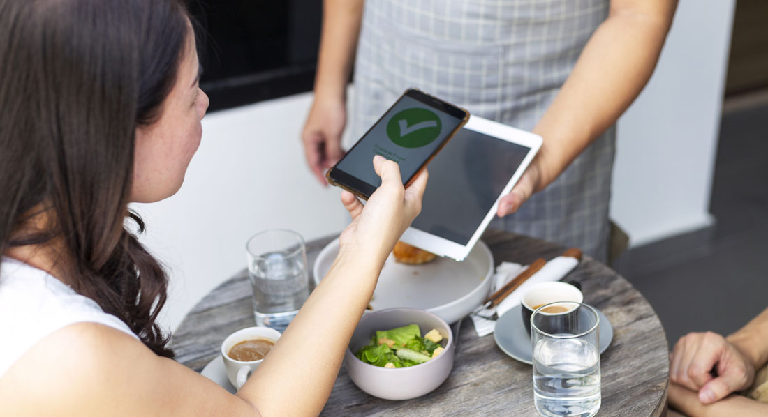 Eine Frau bezahlt in einem Restaurant über die Wallet-App auf ihrem Smartphone