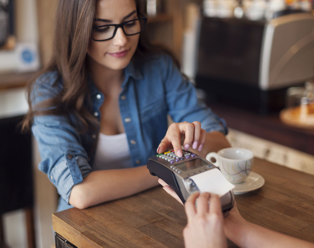 In einem Café tippt eine junge Frau ihre Kreditkarten-PIN in ein Lesegerät