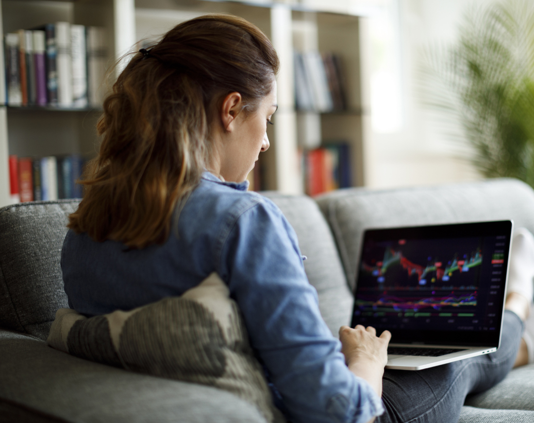 Eine Frau sitzt auf einem Sofa und schaut auf ihrem Laptop Aktienkurse an