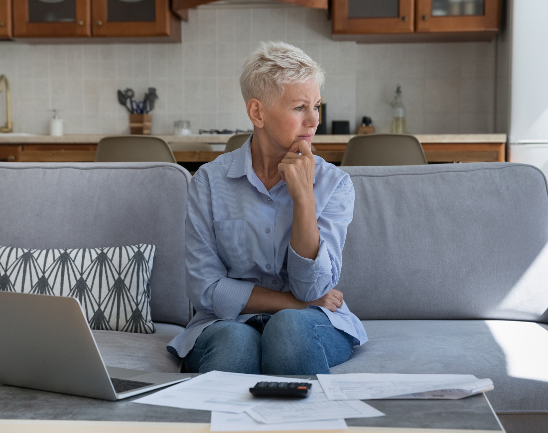 Eine Frau sitzt nachdenklich auf ihrem Sofa vor einem Laptop