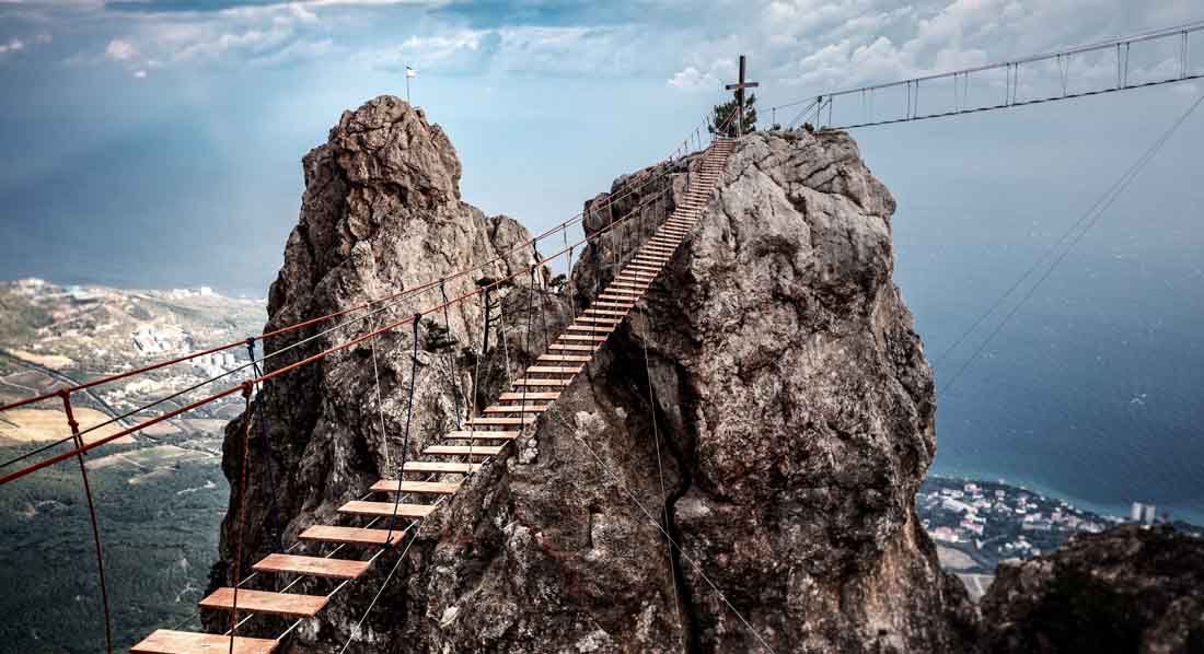 Eine Seilbrücke führt zu einem Berggipfel.