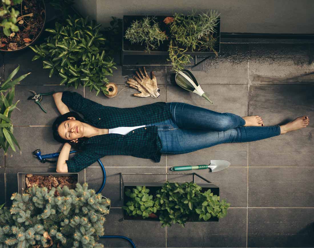 Junge Frau liegt zwischen mehreren Blumenkübeln mit selbst angebauten Pflanzen