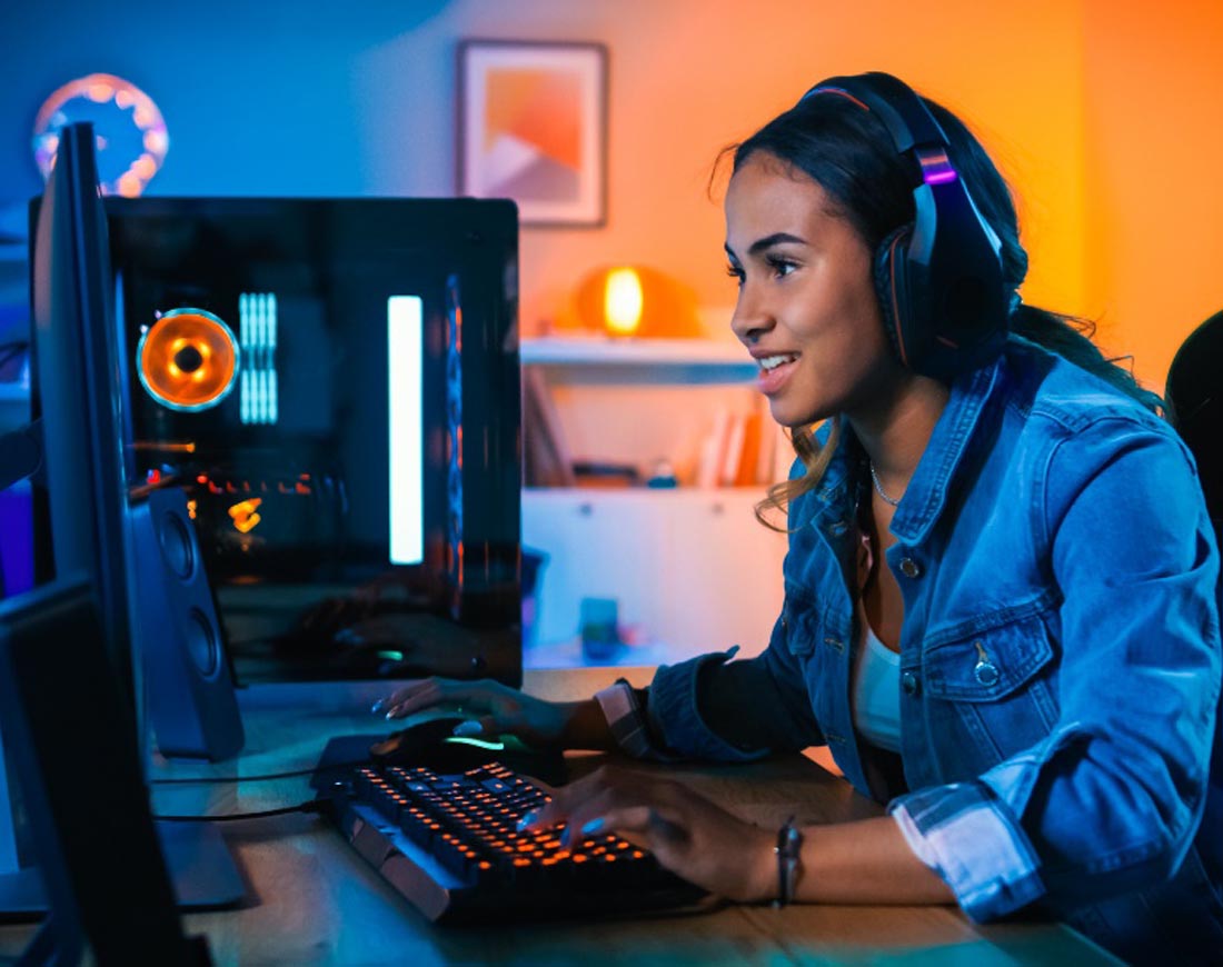 Junge Frau mit Kopfhörern sitzt spielend vor einem Computerbildschirm