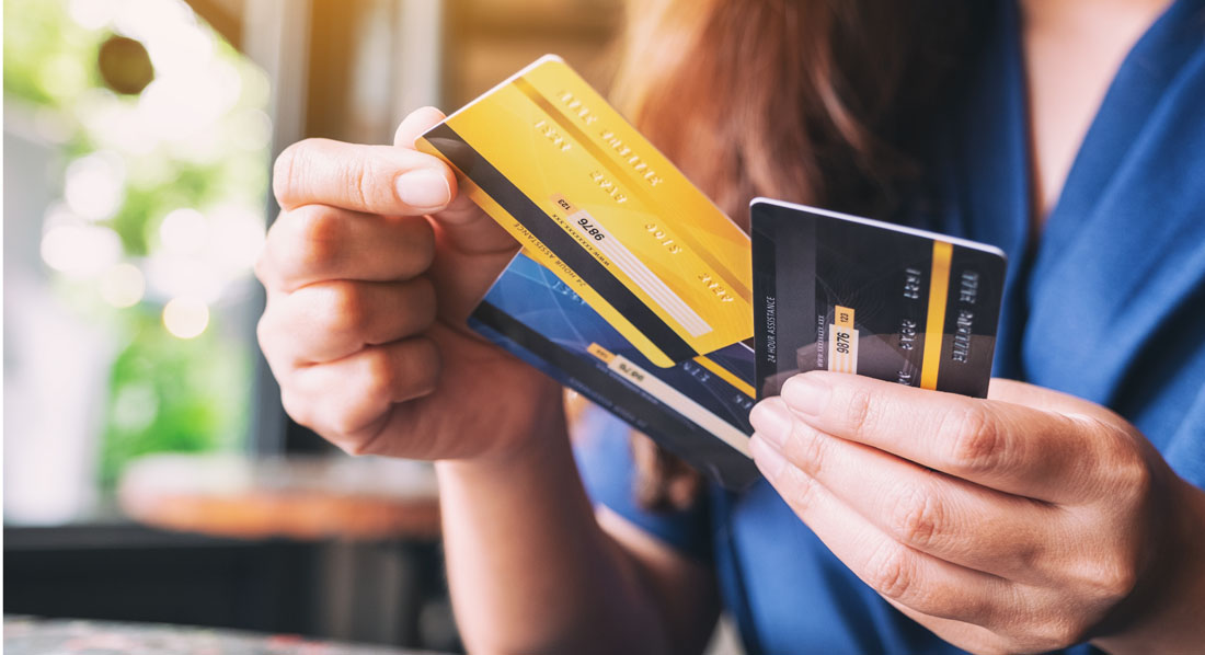 Frau hält drei Kreditkarten in einer Hand und zieht mit der anderen eine der Karten heraus