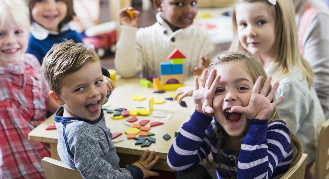 Kindergartenkinder sitzen um einen Tisch und machen Faxen