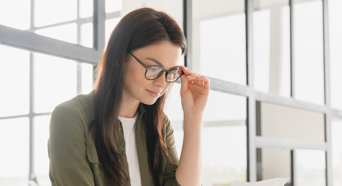 Eine junge Frau mit Brille sitzt in einem hellen Büro und schaut auf ihre Gehaltsabrechnung