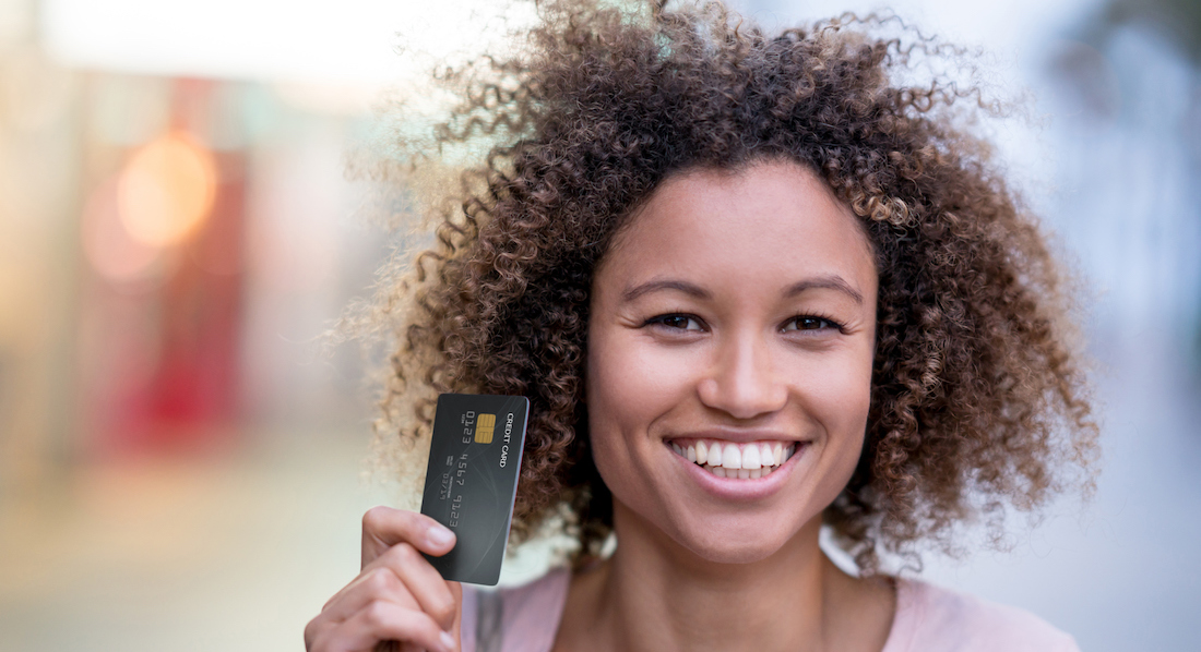 Junge Frau hält lächelnd Kreditkarte in der Hand