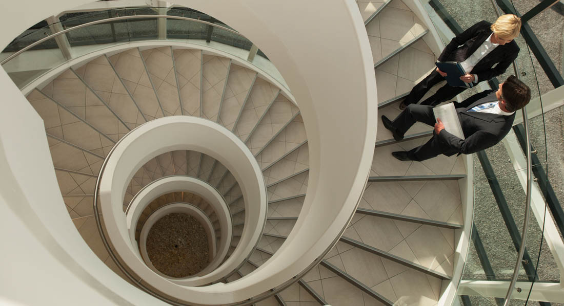 Zwei Geschäftsleute auf einer Wendeltreppe, die nach unten führt