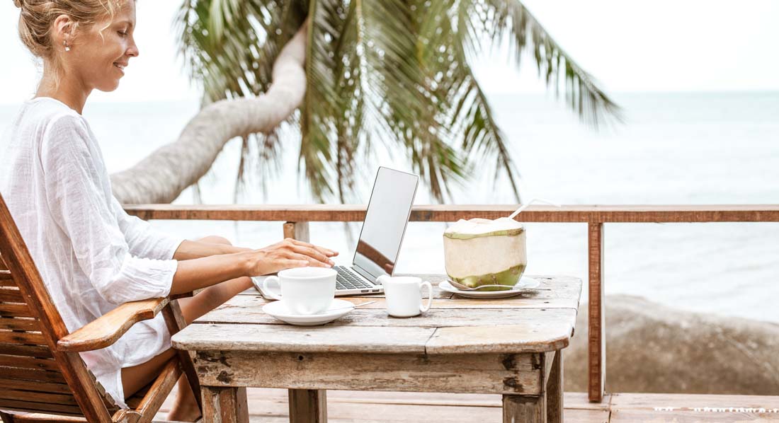 Eine junge Frau arbeitet am Laptop auf einer Terrasse am Meer