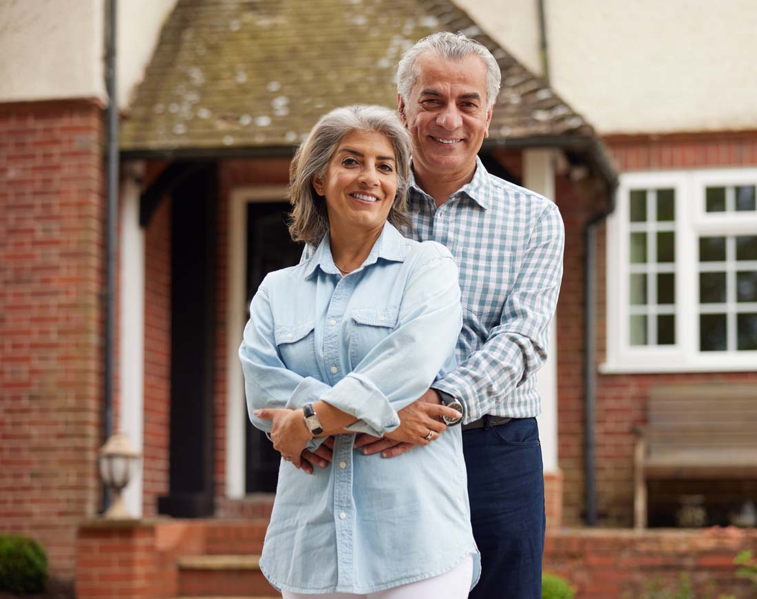 Älteres Paar steht Arm in Arm vor dem eigenen Haus