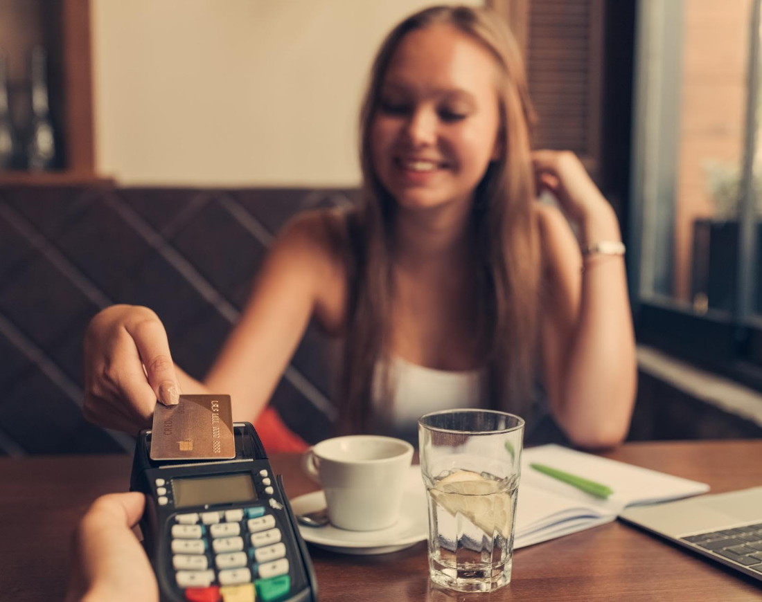 Eine Teenagerin bezahlt in einem Bistro ihren Kaffee mit einer Kreditkarte