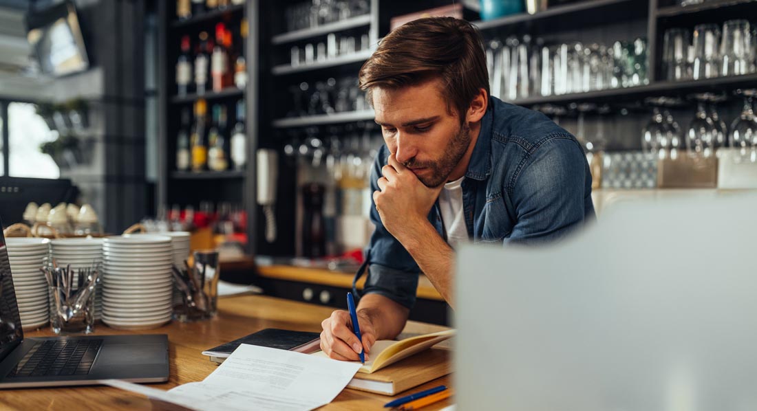 Der Besitzer eines Cafés stützt sich auf den Tresen und rechnet Beträge zusammen