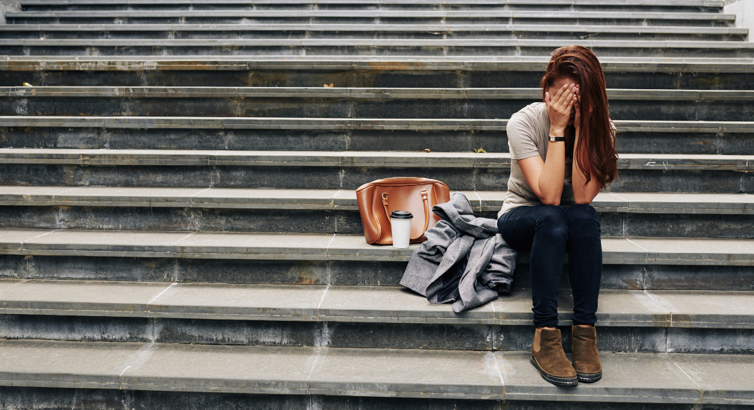 Junge Frau sitzt verzweifelt auf einer öffentlichen Treppe
