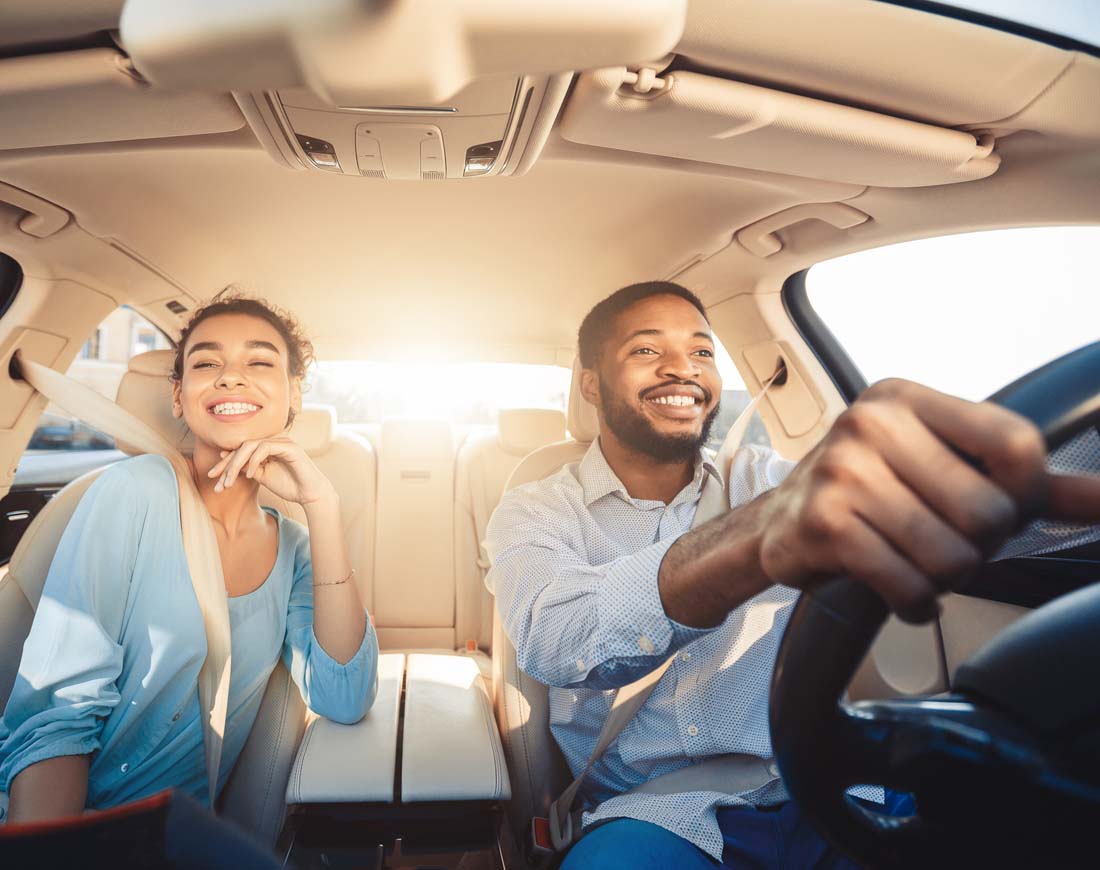Eine junges Paar fährt lachend in seinem neuen Auto