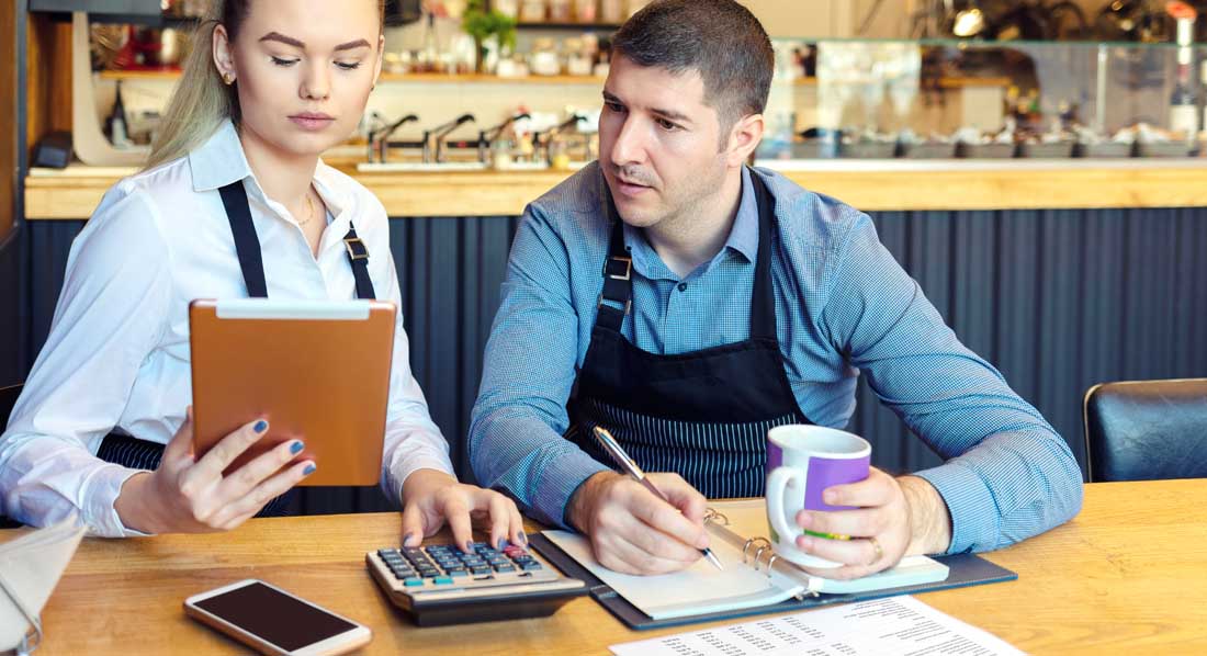 Junges Paar am Tisch ihres Restaurants kalkulieren die Zuschüsse zur Selbstständigkeit