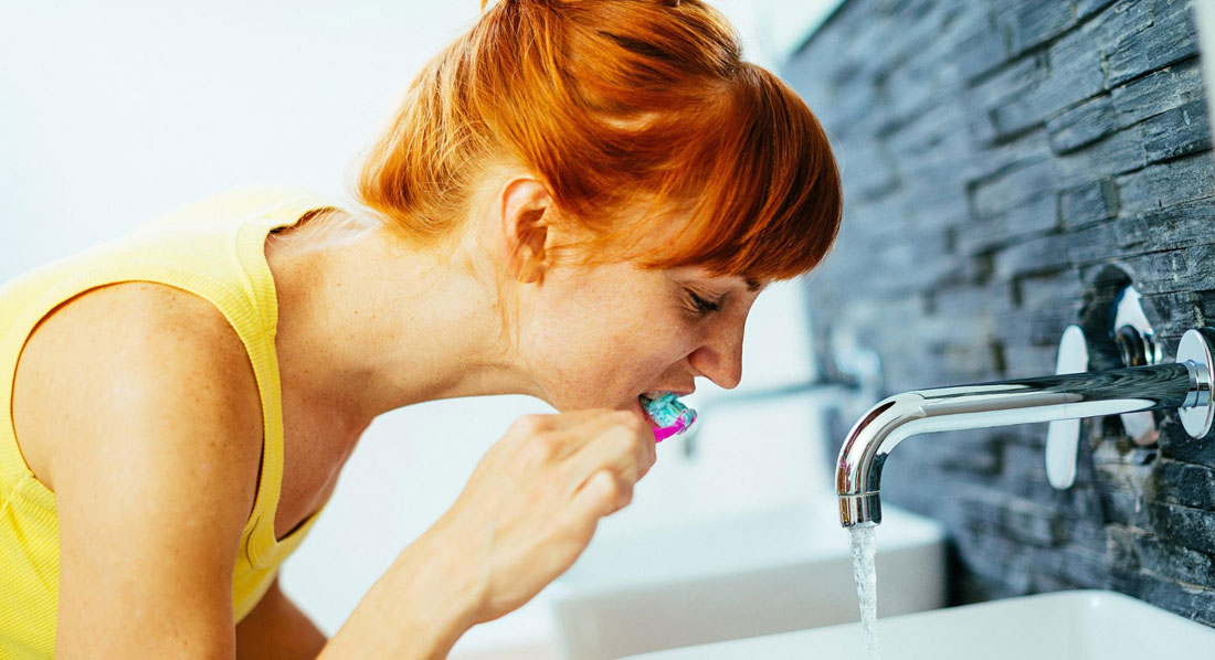 Eine junge Frau putzt Zähne bei laufendem Wasserhahn
