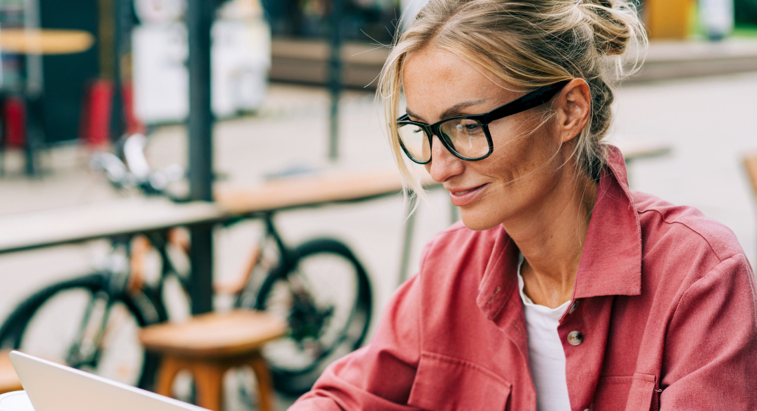 Eine Frau sitzt in einem Café und arbeitet mit einer Bezahlkarte in der Hand an einem Laptop