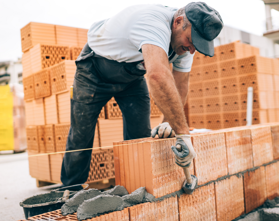 Handwerker mit Kappe mauert in Schwarzarbeit eine Wand eines neuen Hauses
