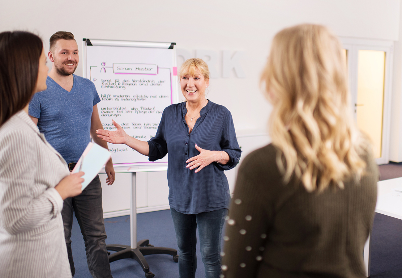 Vier Personen steht vor einem Flipchart. Die Person in der Mitte erklärt etwas.