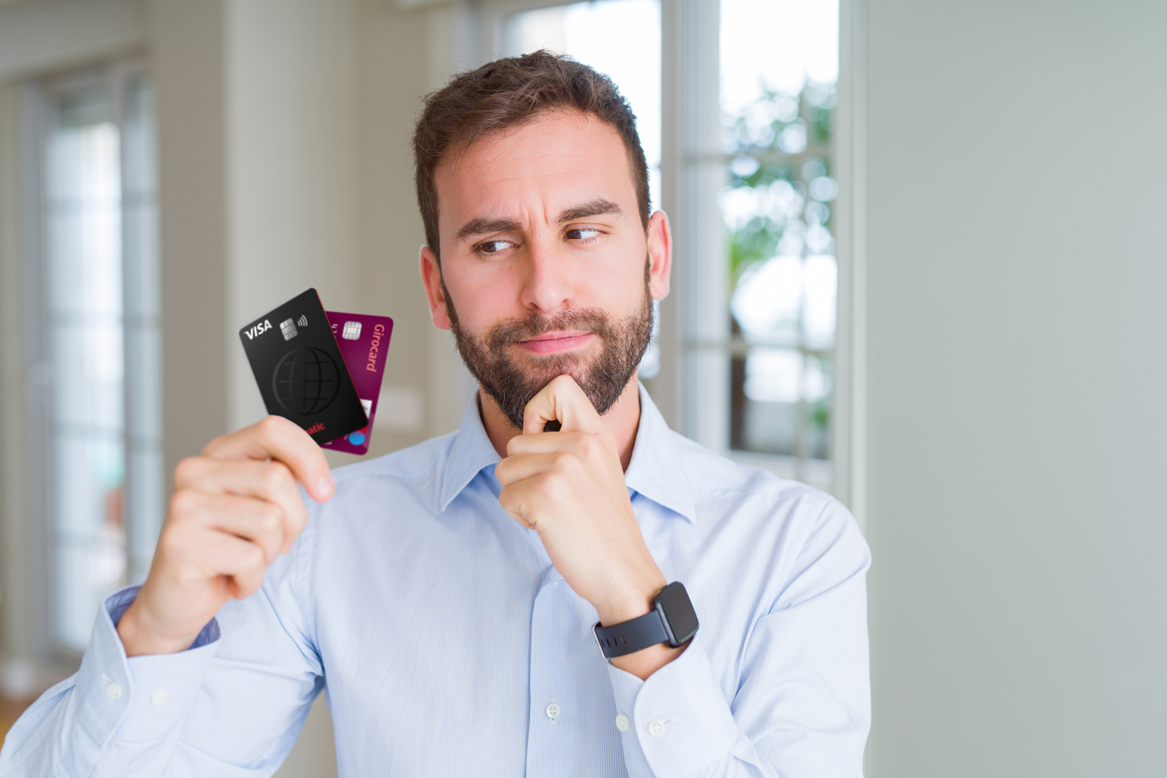 Mann sieht grübelnd auf Kredit- und Girokarten in seiner Hand