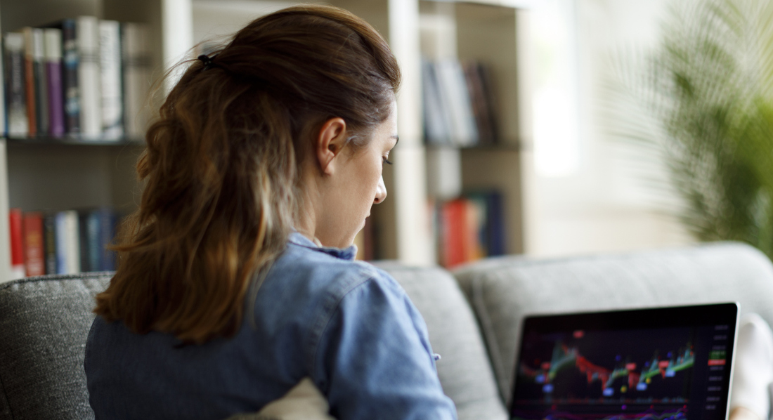 Eine Frau sitzt auf einem Sofa und schaut auf ihrem Laptop Aktienkurse an