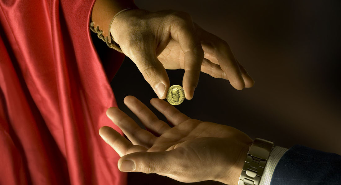 Mann in Kleidung alter Römer übergibt Münze an Mann in modernem Anzug