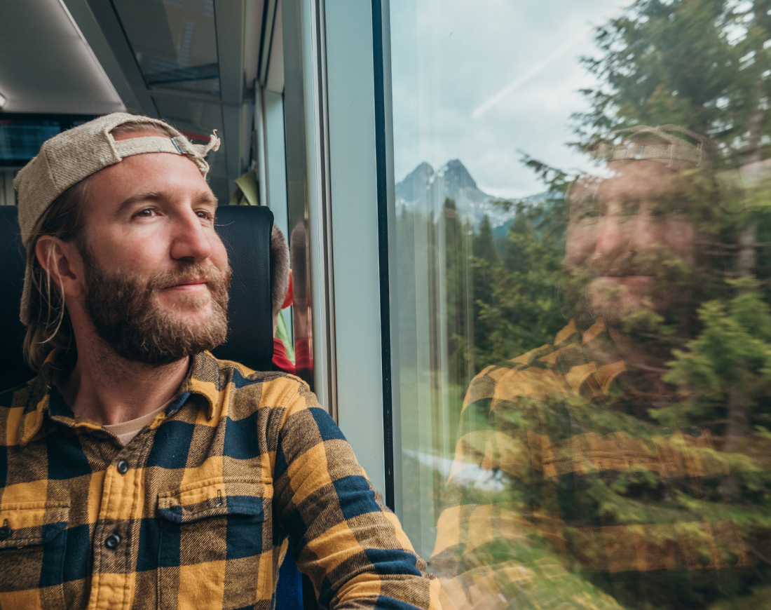 Ein Mann sitzt im Zug, der durch einen Wald fährt, und genießt die Landschaft durch das Fenster